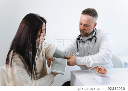 Male doctor puts on the arm of the female patient the cuff of blood pressure monitor Male doctor puts on the arm of the female patient the cuff of blood pressure monitor 92859010
