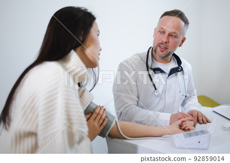 The male doctor measures the woman blood pressure and records the results in the patient's card. Female at the appointment at cardiologist 92859014