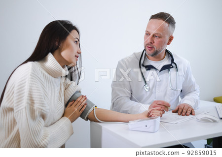 The male doctor measures the woman blood pressure and records the results in the patient's card. Female at the appointment at cardiologist 92859015