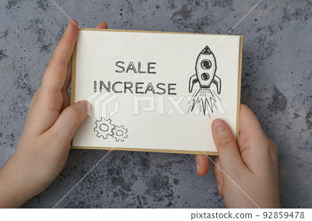 Woman holds card with words Sale Increase on concrete 92859478