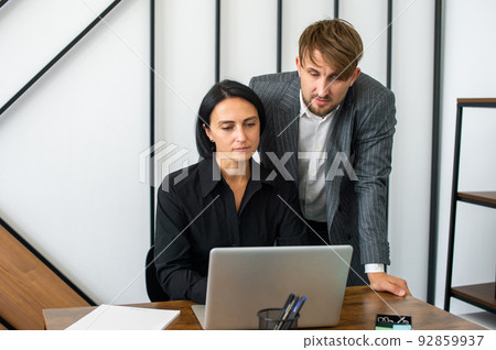 a man and a woman in the office are working at a laptop and smiling 92859937