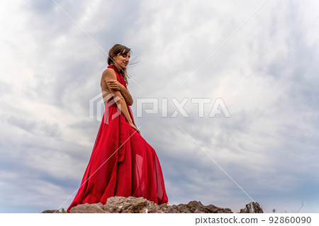 A woman in a red dress stands above a stormy sky, her dress fluttering, the fabric flying in the wind. A woman in a red dress stands above a stormy sky, her dress fluttering, the fabric flying in the wind. 92860090