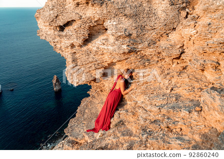 A girl with loose hair in a red dress stands on a rock rock above the sea. In the background, the sea and the rocks. The concept of travel 92860240
