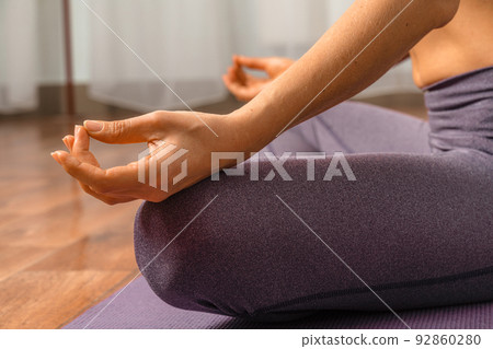 Young woman meditating in the lotus pose at home. Practicing yoga indoors. Harmony, yoga practice, balance, meditation, relaxation at home, healthy lifestyle concept. 92860280
