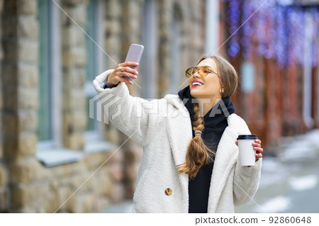 Young stylish woman with smartphone and coffee outdoor. She make a selfie. 92860648