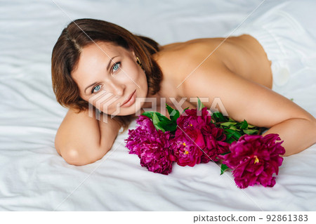attractive brunette topless woman with a bouquet of peonies on the bed. 92861383