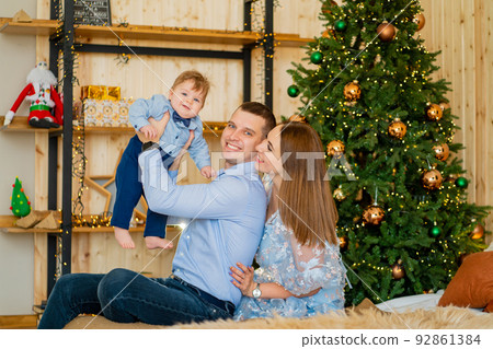 dad holds young son in hands, and mom sits next on the bed by the Christmas tree dad holds young son in hands, and mom sits next on the bed by the Christmas tree 92861384