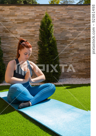 young woman practising meditation in the garden in the open air, relaxation exercises, doing the lotus posture. vertical. concept of health and well-being. young woman practising meditation in the garden in the open air, relaxation exercises, doing the lotus posture. vertical. concept of health and well-being. 92861498