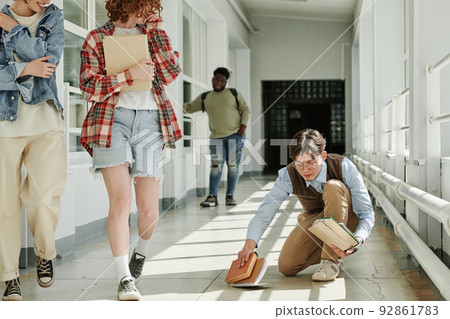 Youthful Asian guy picking fallen books from the floor in college corridor Youthful Asian guy picking fallen books from the floor in college corridor 92861783