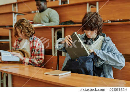 Teenage brunette girl in casualwear putting book into backpack after lesson 92861834