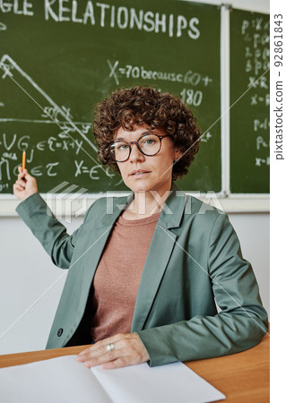 Confident teacher of geometry pointing at drawing of triangle on blackboard 92861843
