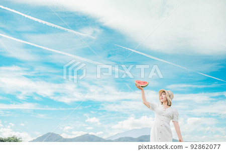 A woman in a white dress holding a watermelon under the blue sky A woman in a white dress holding a watermelon under the blue sky 92862077
