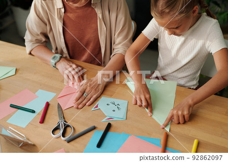 Creative youthful girl and her mother folding paper while making origami Creative youthful girl and her mother folding paper while making origami 92862097