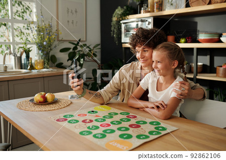 Smiling young woman with smartphone making selfie with her daughter 92862106