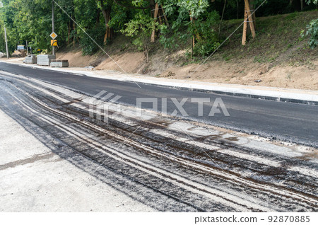 Laying a new asphalt on the road. Layer of fresh hot asphalt on the street. 92870885
