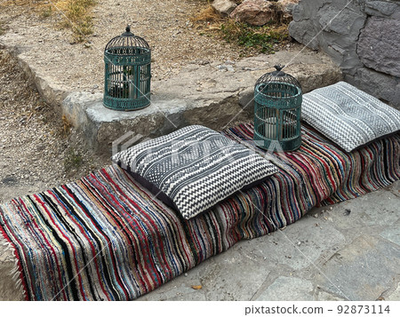 Vintage metal birdcages outdoors on a carpet with cushions. Vintage metal birdcages outdoors on a carpet with cushions. 92873114