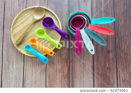 Set of plastic measuring spoon and measuring cups in various color on wooden plate in top view 92874062