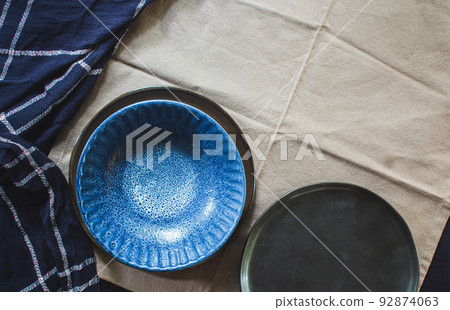 Empty vintage round dishes set on light brown cloth background. Styling with blue texture cloth. 92874063