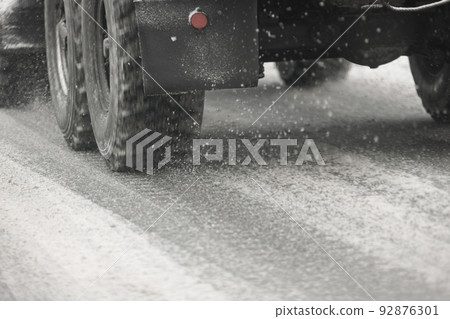 Road snow pieces flow from wheels of russian military truck moving on daylight city with selective focus 92876301