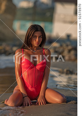 Brunette girl with silicone boobs in swimsuit posing on the beach, kneeling 92878970