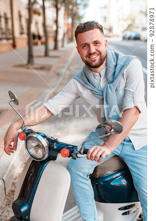 Portrait of a young and stylish man with a moped in summer sunny day in european city 92878971