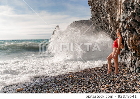 A beautiful and sexy brunette in a red swimsuit on a pebble beach, Running along the shore in the foam of the waves A beautiful and sexy brunette in a red swimsuit on a pebble beach, Running along the shore in the foam of the waves 92879541