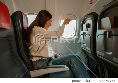 Smiling woman closing window during flight on plane Smiling woman closing window during flight on plane 92879578