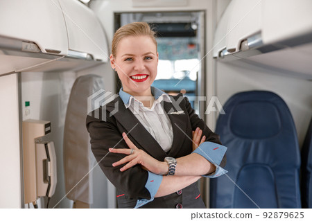Cheerful stewardess standing in passenger airline cabin Cheerful stewardess standing in passenger airline cabin 92879625