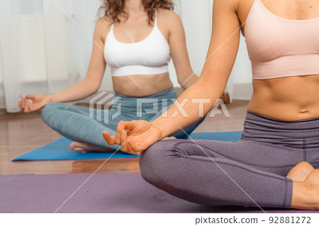 Two attractive athletic girls train asana yoga pose on mats on a light background. A group of young women stretch out in the gym. Healthy lifestyle concept 92881272