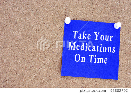Take your medications on time text on stick note on a cork notice board. 92882792