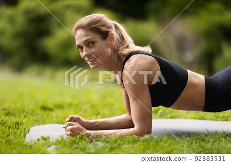 Side view of pretty sporty woman planking at public park Side view of pretty sporty woman planking at public park 92883531