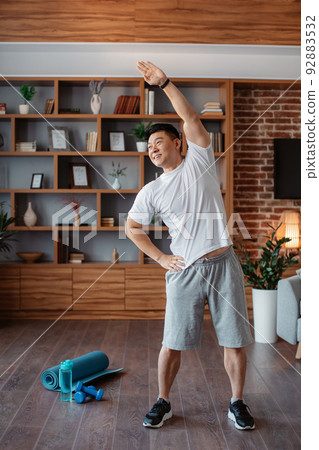 Active asian mature man in sportswear doing exercise and warm-up in living room interior, crop, copy space 92883532