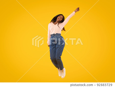 Joyful african american lady jumping in air and looking at camera, woman having fun over yellow studio background 92883729