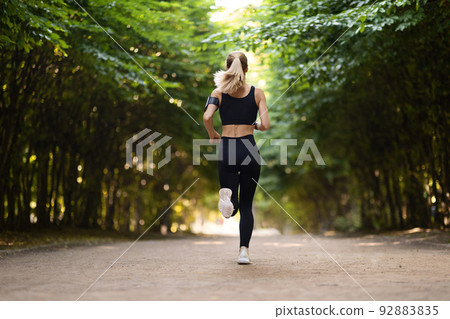Slim woman in sportswear jogging by park, back view 92883835