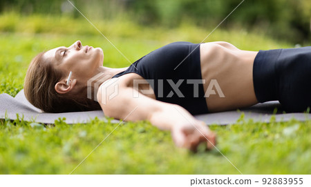 Relaxed woman laying on fitness mat, meditating 92883955