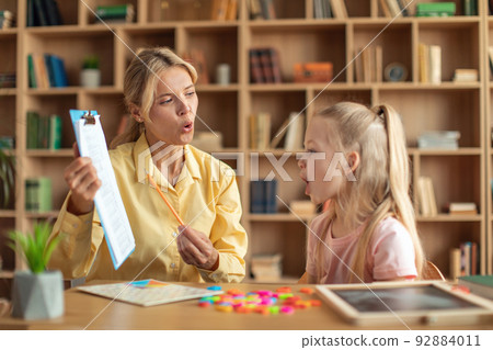 Cheerful female speech therapist curing girl's problems and impediments, cute child learning and pronouncing letters 92884011