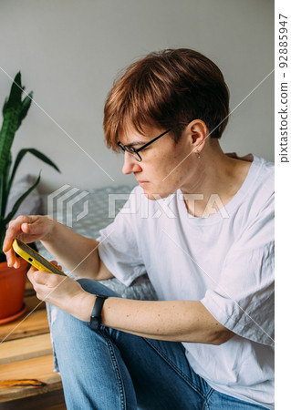 Woman with short hair at home sitting on the floor with her smartphone 92885947