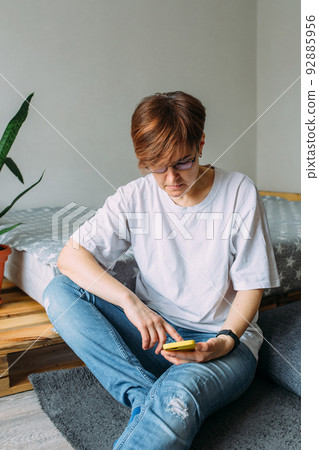 Woman with short hair at home sitting on the floor with her smartphone 92885956