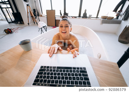 Young woman working on laptop while taking a bathtub Young woman working on laptop while taking a bathtub 92886379
