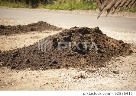 Bucket of excavator pours out the ground against the background of a rural industrial zone. Bulldozer work on the construction site 92886415