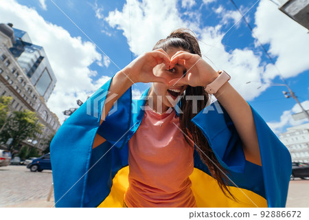 Young woman with Ukrainian flag shows heart with hands Young woman with Ukrainian flag shows heart with hands 92886672