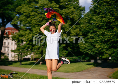 Young woman waving LGBT pride flag in the park. 92886679