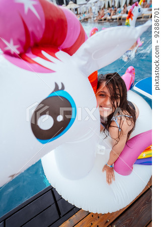 Happy young woman sitting on inflatable unicorn toy mattress Happy young woman sitting on inflatable unicorn toy mattress 92886701
