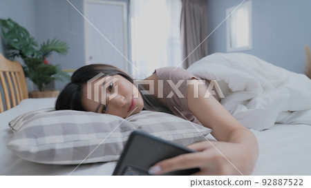 Holiday concept of 4k Resolution. Asian girls don't want to get out of bed in the morning. Mobile phone alarm. Laziness in waking up. 92887522