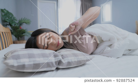 Holiday concept of 4k Resolution. Asian girls don't want to get out of bed in the morning. Mobile phone alarm. Laziness in waking up. 92887524