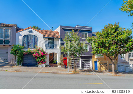 Sloped row of houses in San Francisco, California with trees and plants near the sidewalk 92888819