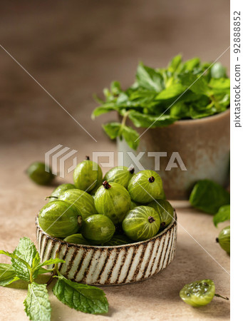 Fresh gooseberry in ceramic bowl with mint leaves on beige textured background with copy space. Close up. Raw healthy dessert. Fresh gooseberry in ceramic bowl with mint leaves on beige textured background with copy space. Close up. Raw healthy dessert. 92888852