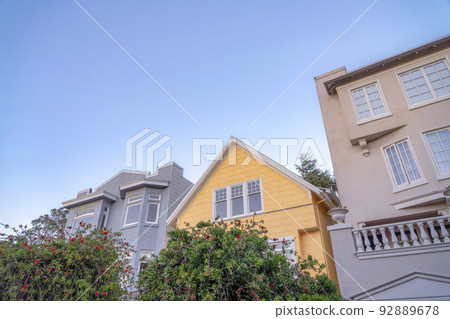 Yellow gable house in the middle of two houses with painted concrete wall exterior 92889678