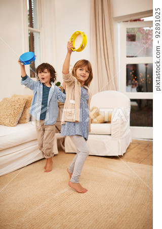 Making fun with music. Shot of two young children playing with tambourines in the living room at home. 92891025