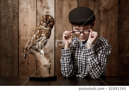 Knowledge is the key. Young boy in retro clothing wearing spectacles with a stern expression alongside an owl. Knowledge is the key. Young boy in retro clothing wearing spectacles with a stern expression alongside an owl. 92891393